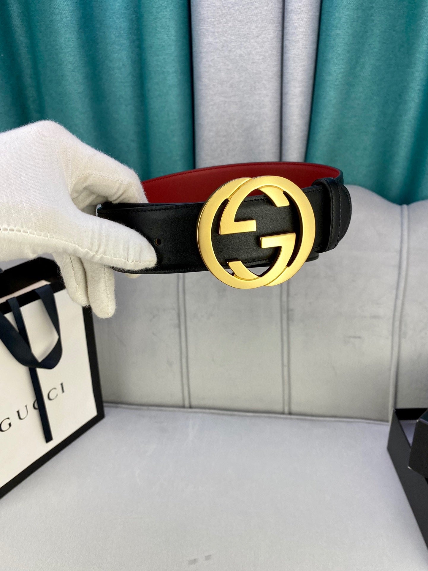Black leather belt held by hand with gold-toned GG buckle and red interior