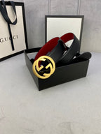 Black leather belt with gold-toned GG buckle, red underside lining