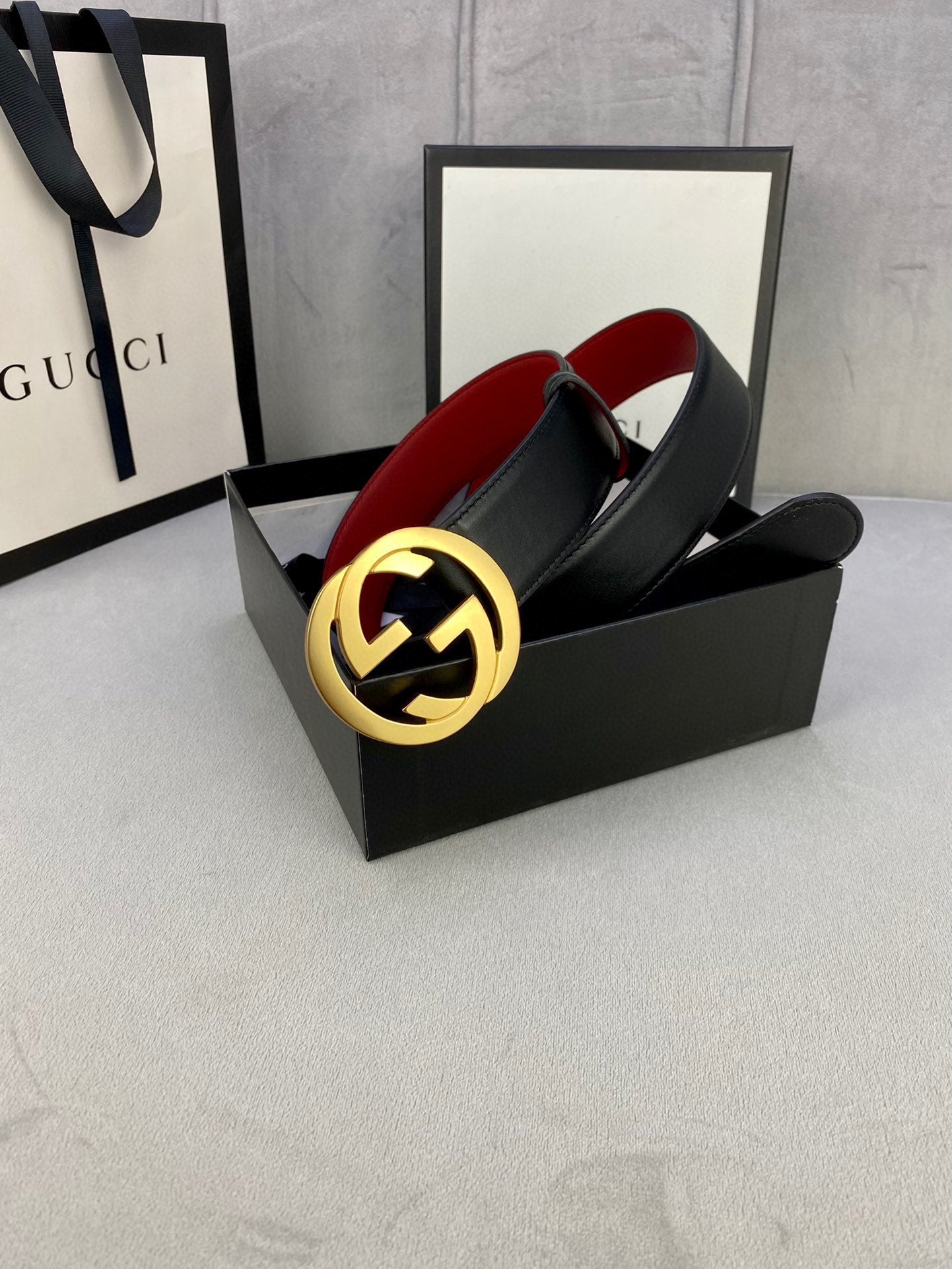 Black leather belt with gold-toned GG buckle, red underside lining