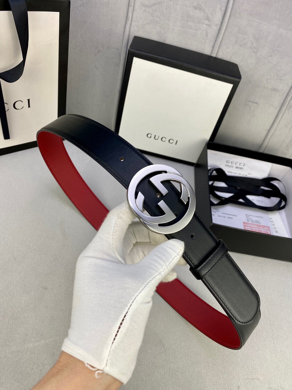 Black leather belt with silver GG buckle, red underside, hand holding the strap