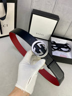 Black leather belt with silver GG buckle, red underside, hand holding the strap