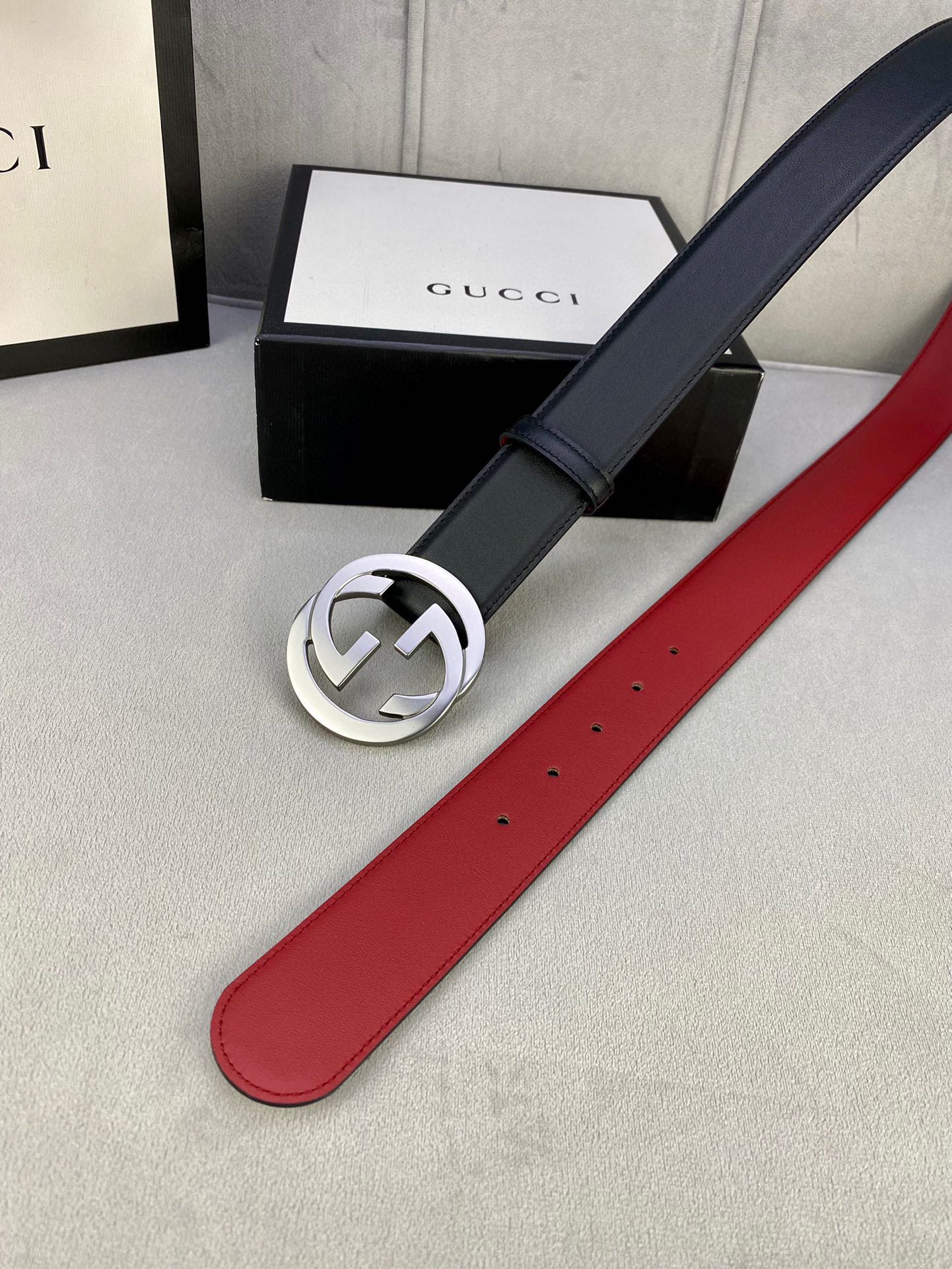 Black leather belt with silver GG buckle, red underside and punched holes, side view