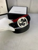 Black leather belt with silver GG buckle held in white glove, red lining visible