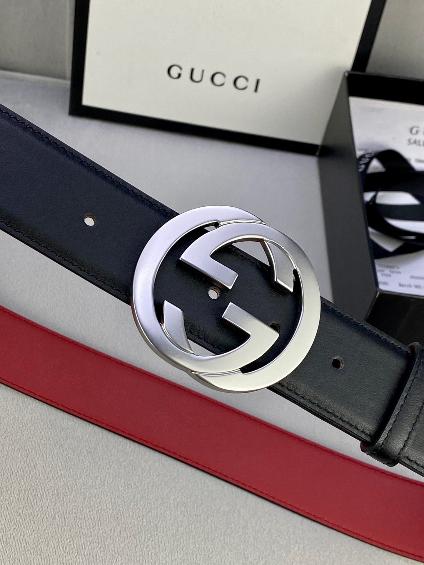 Dark leather belt with silver GG buckle and red trim, close-up on buckle