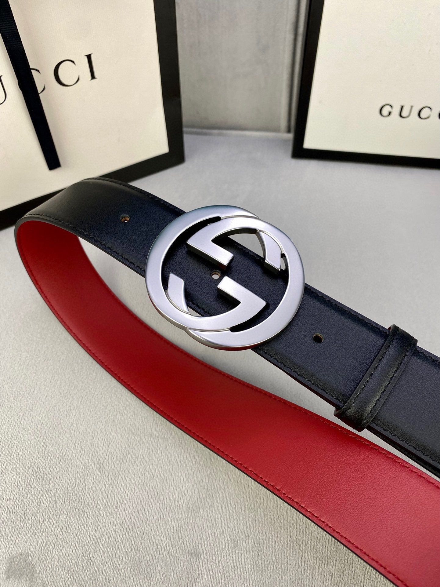 Dark leather belt with silver GG buckle and red underside, angled view on display