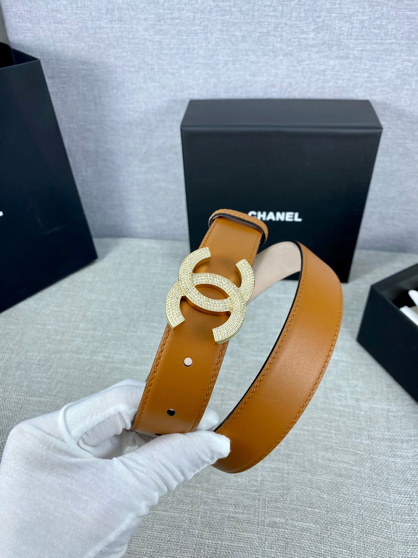Tan leather belt close-up with rhinestone CC buckle and round metal hole marks