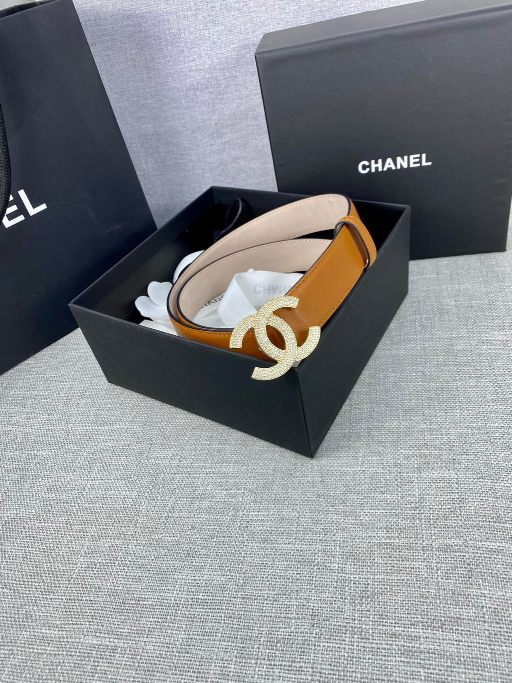 Tan leather belt in box with rhinestone CC buckle on a curved strap