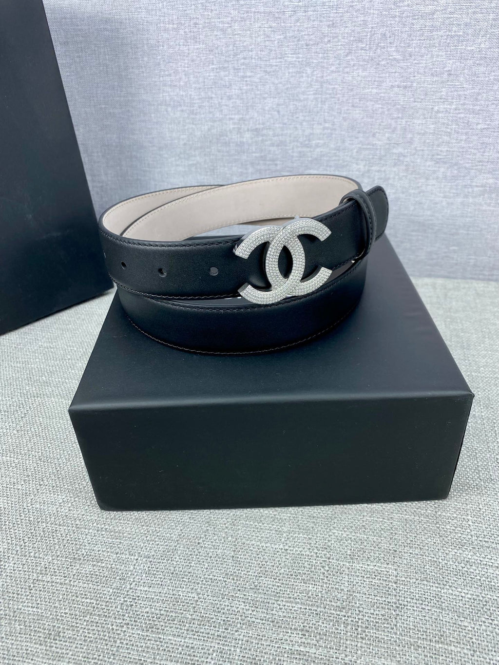 Black leather belt with silver-tone CC buckle on a dark box base