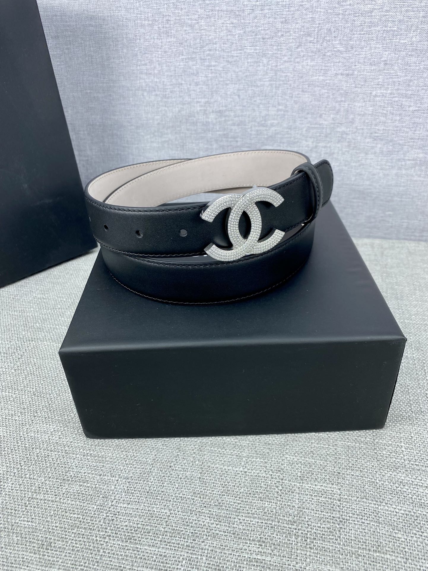Black leather belt with silver-tone CC buckle on a dark box base