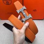 Hermes belt held in hand: orange leather strap with wide H buckle on black backing