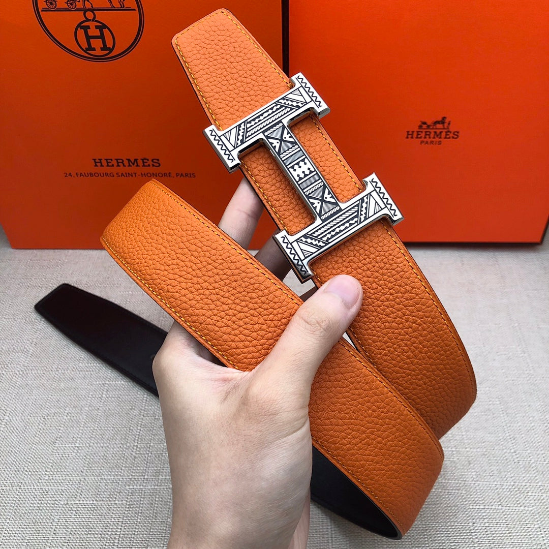 Hermes belt held in hand: orange leather strap with wide H buckle on black backing