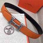 Hermes belt with orange leather strap and ornate gold-tone H buckle, black reverse side