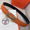 Hermes belt with orange textured leather strap and gold-tone H buckle on black backing