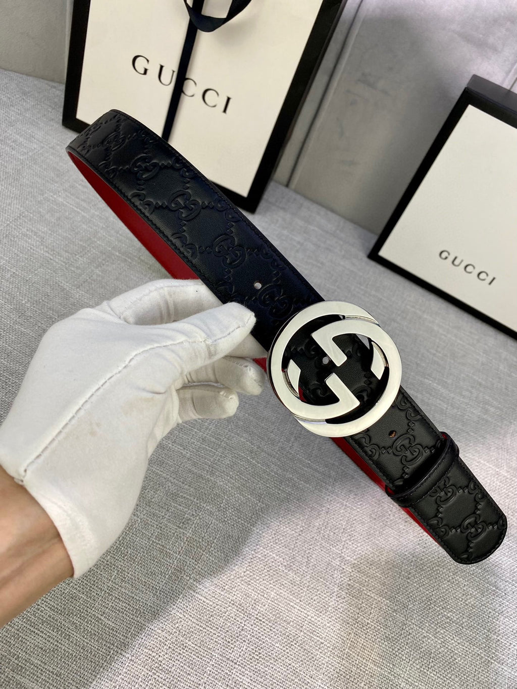 Gucci belt worn with black embossed leather and silver-tone GG buckle, red underside