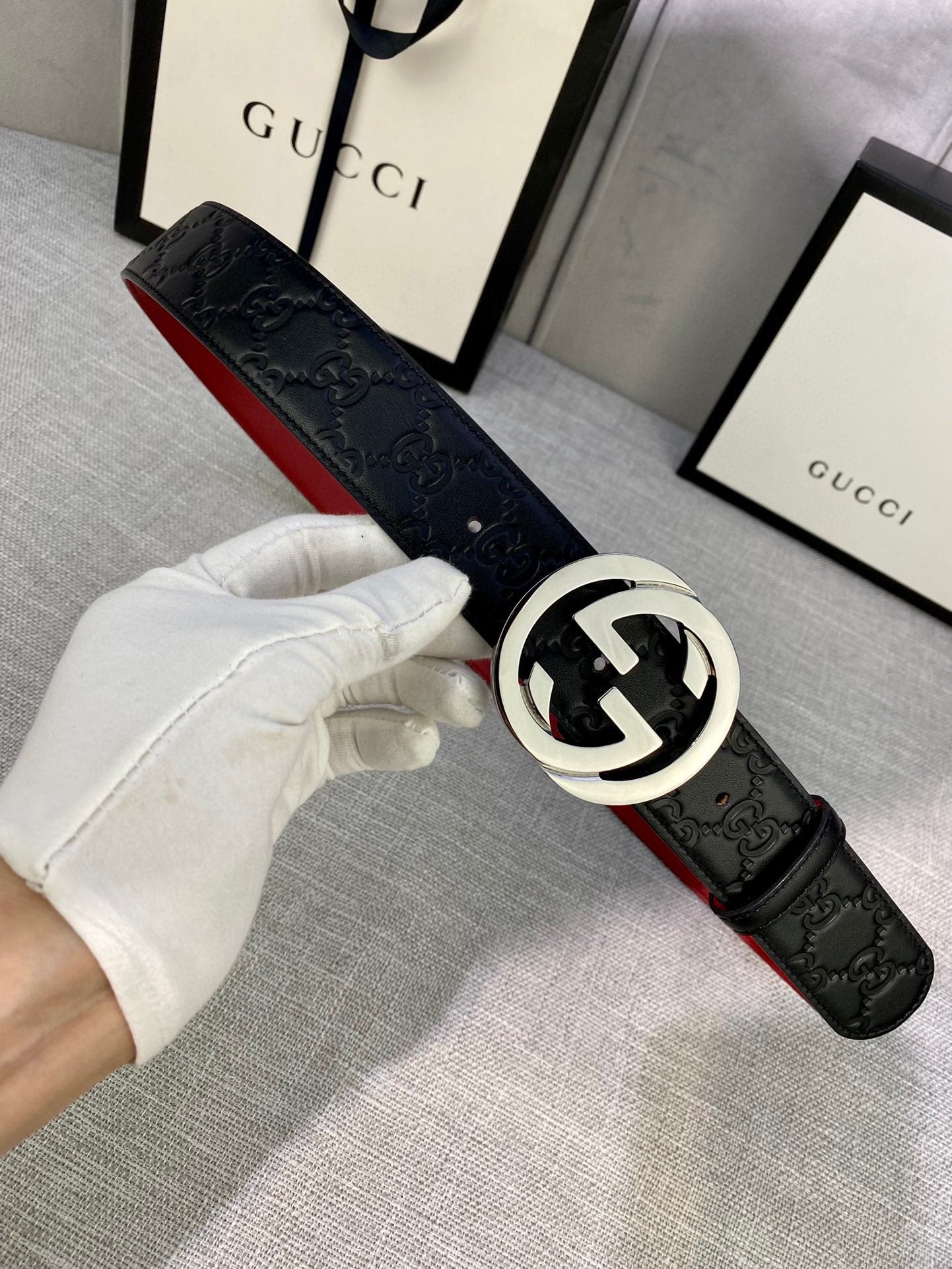 Gucci belt worn with black embossed leather and silver-tone GG buckle, red underside