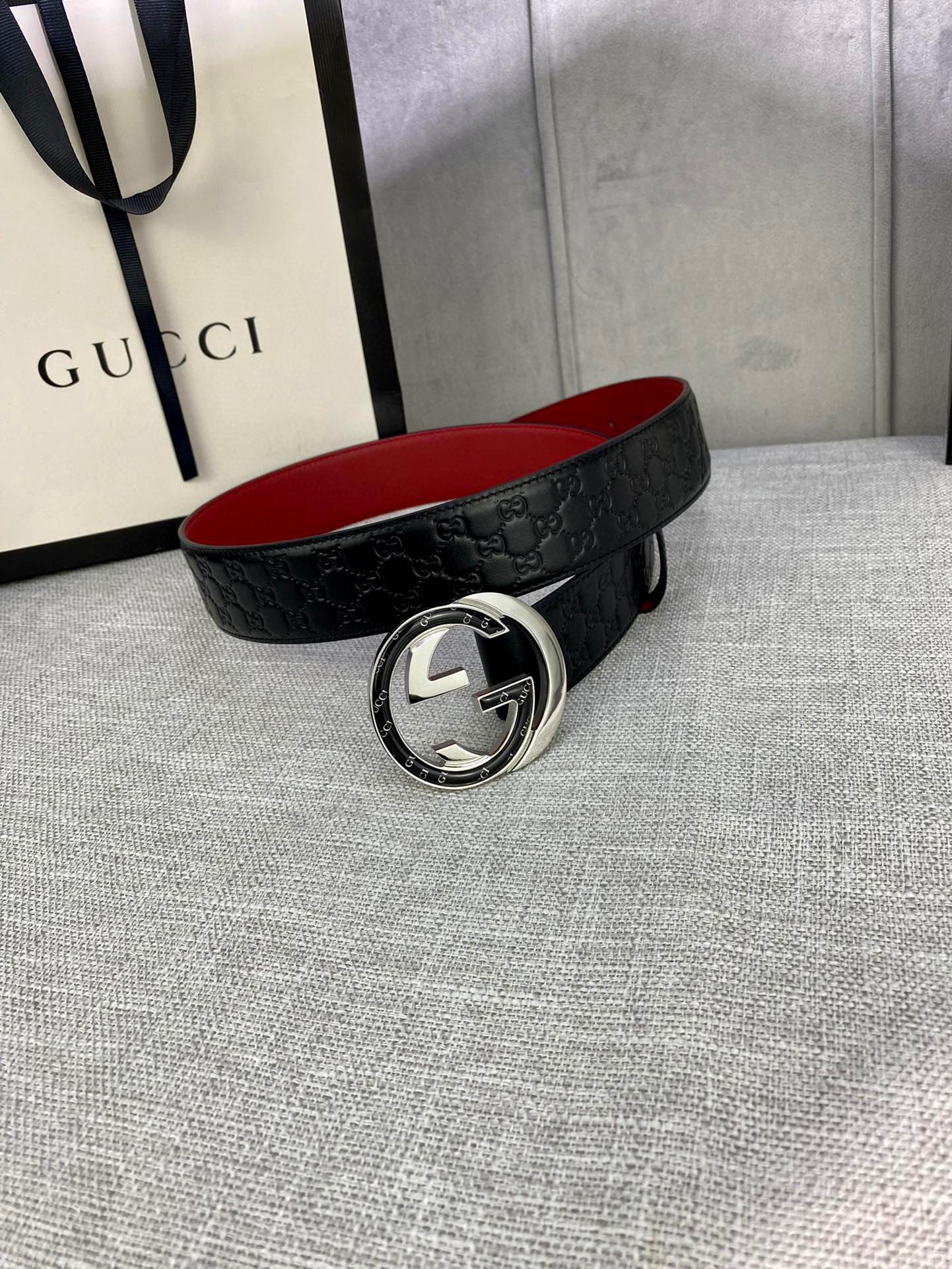Gucci belt lying flat: black GG-pattern leather with silver buckle and red inner side