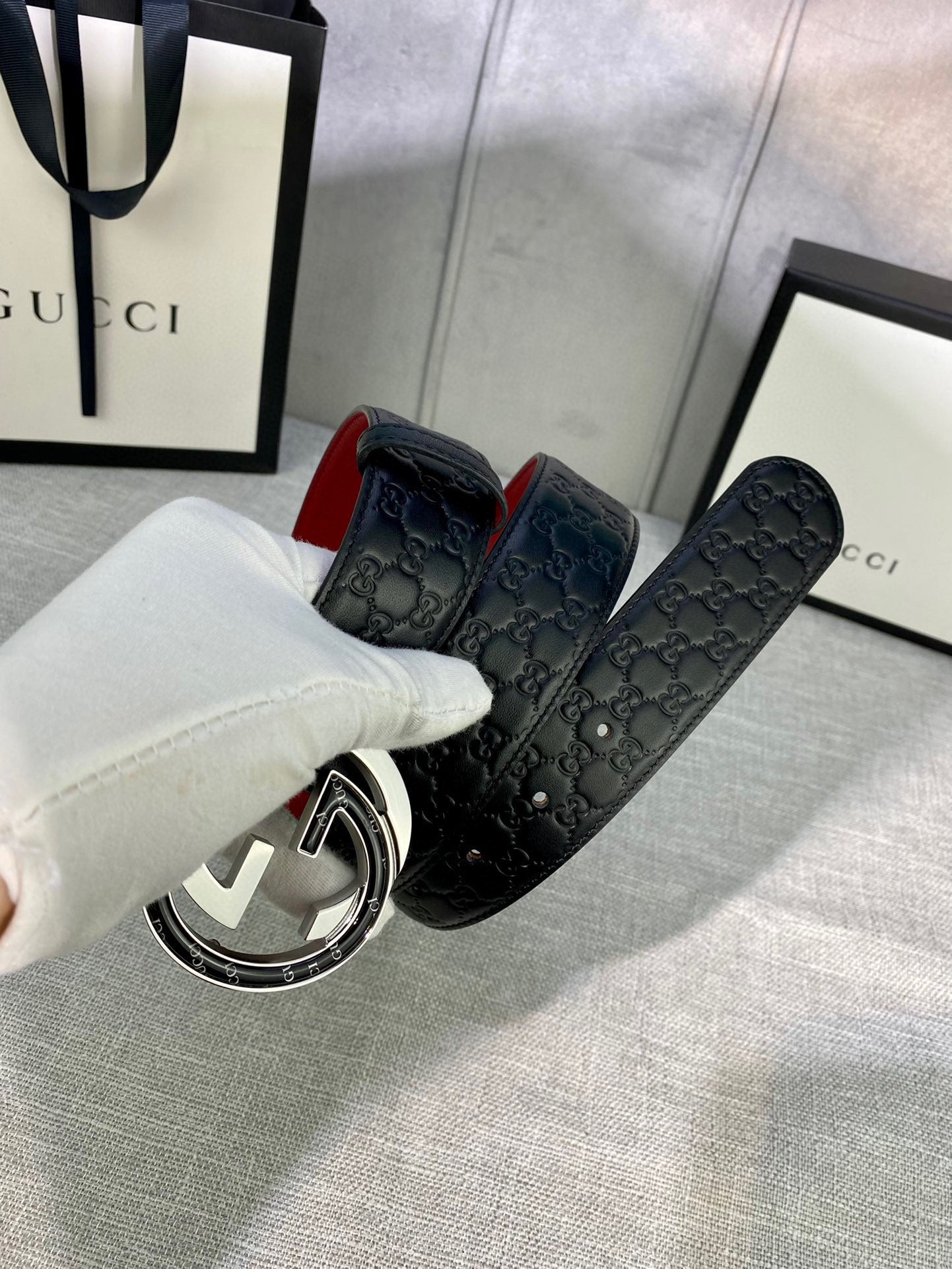 Gucci belt detail held in hand: black GG leather with red underside and silver buckle