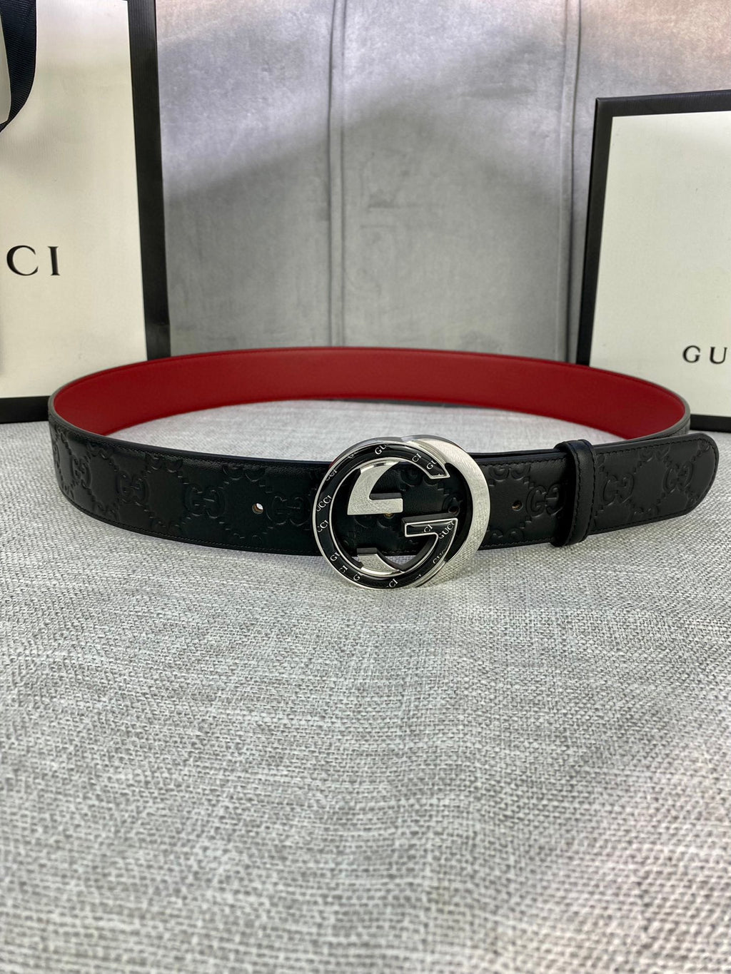 Black leather Gucci-logo belt with round GG emblem buckle; red underside visible