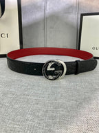 Black leather Gucci-logo belt with round GG emblem buckle; red underside visible