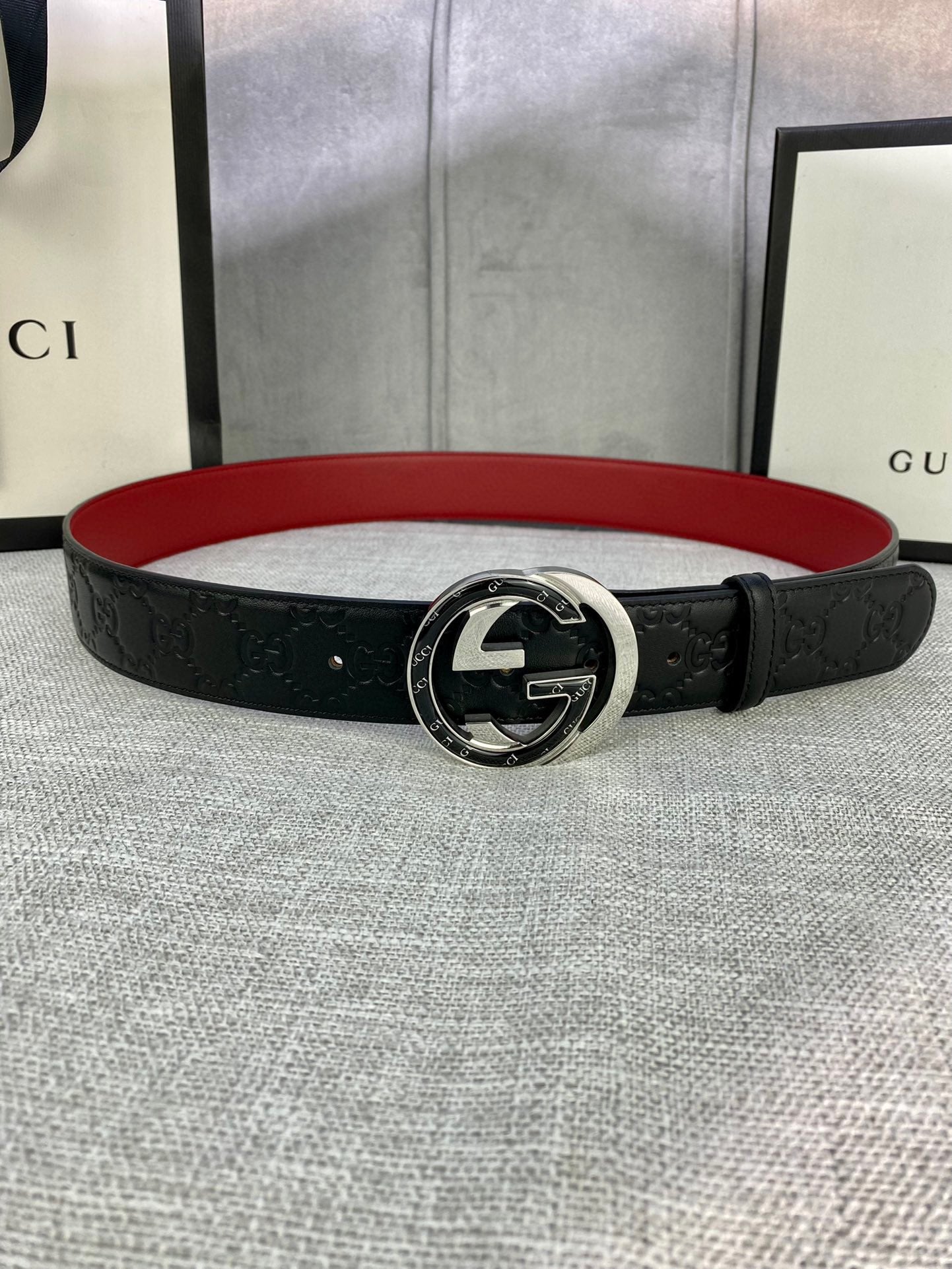 Black leather Gucci-logo belt with round GG emblem buckle; red underside visible