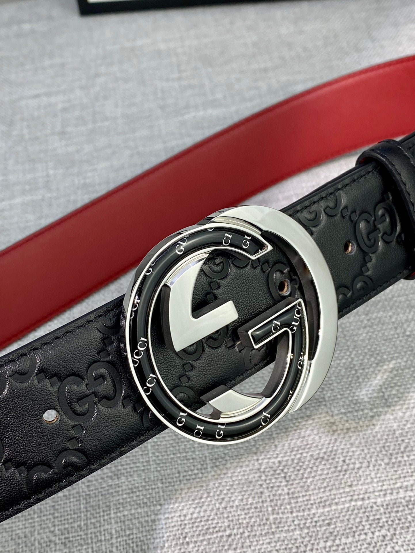 Black Gucci-logo belt close-up with round silver-tone buckle and red lining