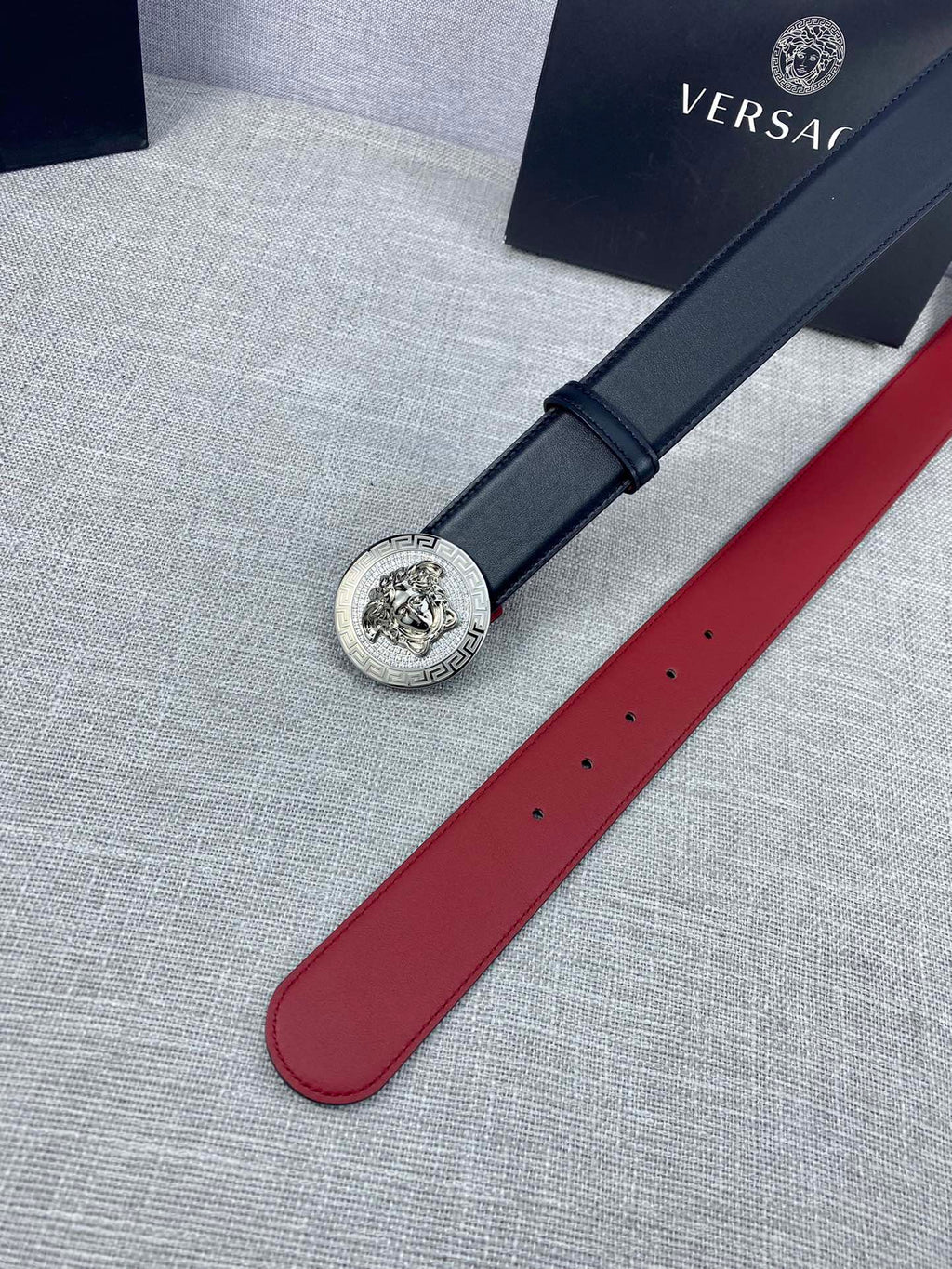 Versace leather belt laid flat: round gold Medusa-style buckle on dark blue strap with holes