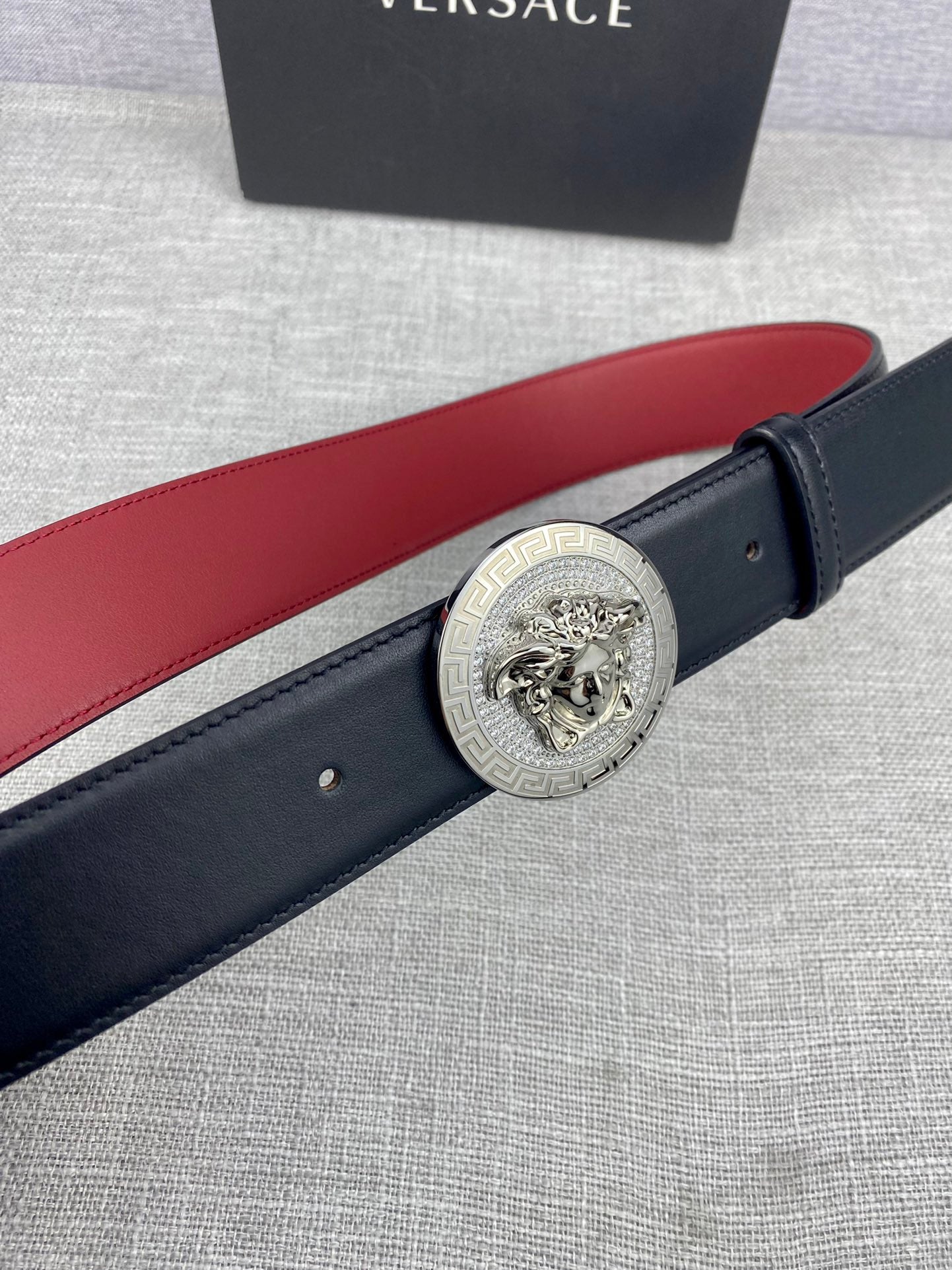 Versace leather belt close-up: round gold Medusa-style buckle on dark strap with red lining