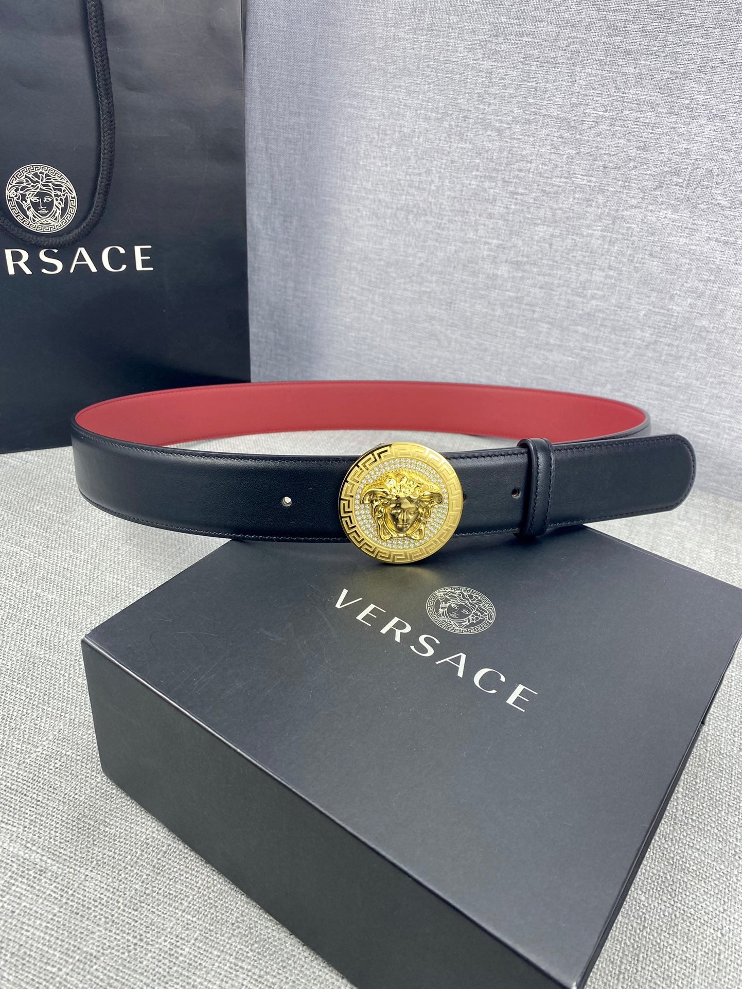 Versace leather belt on a box: dark strap with red underside and large gold Medusa-style buckle