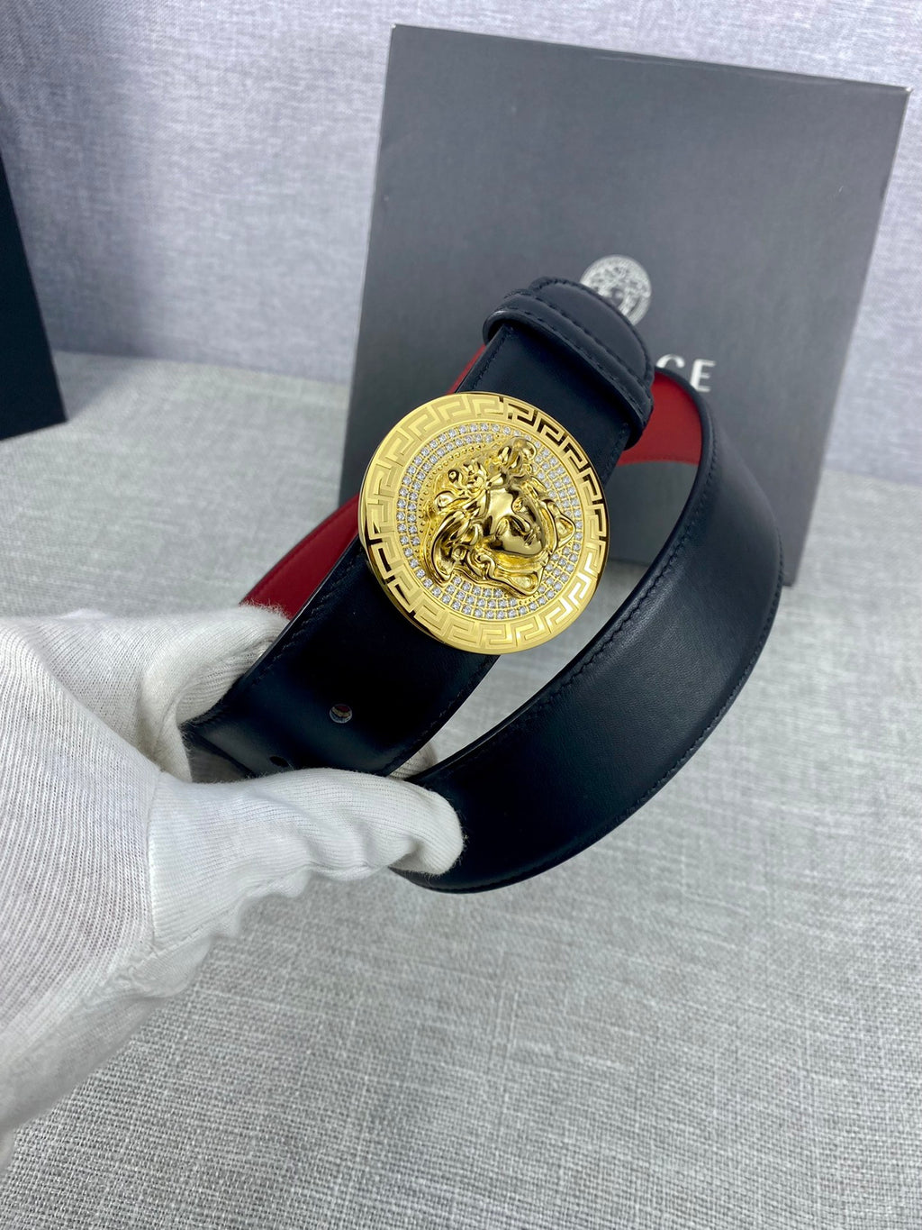 Versace leather belt close-up in hand: gold Medusa-style buckle on dark strap with red lining