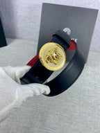 Versace leather belt close-up in hand: gold Medusa-style buckle on dark strap with red lining