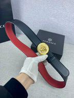 Versace leather belt held by hand: dark strap with red underside and round gold Medusa-style buckle