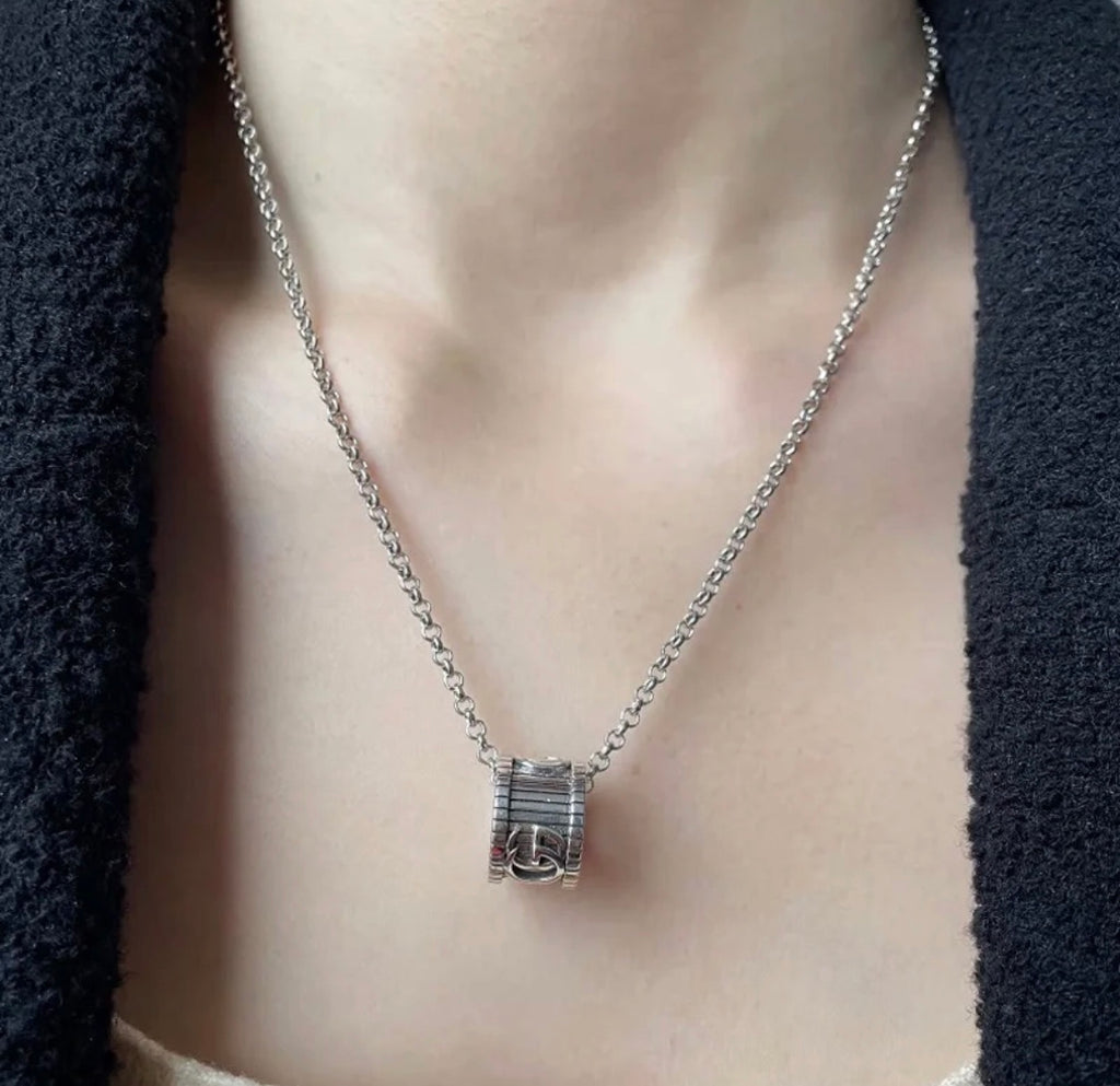 Gucci necklace close-up: silver logo pendant on chain, on neckline