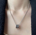 Gucci necklace close-up: silver logo pendant on chain, on neckline