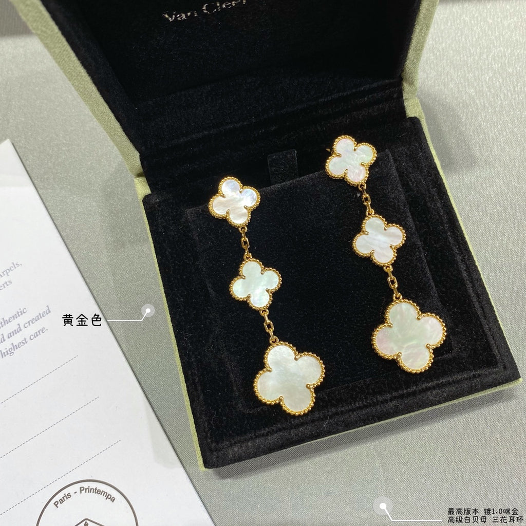 Gold clover dangle earrings with three linked four-leaf motifs and pale inlay accents.