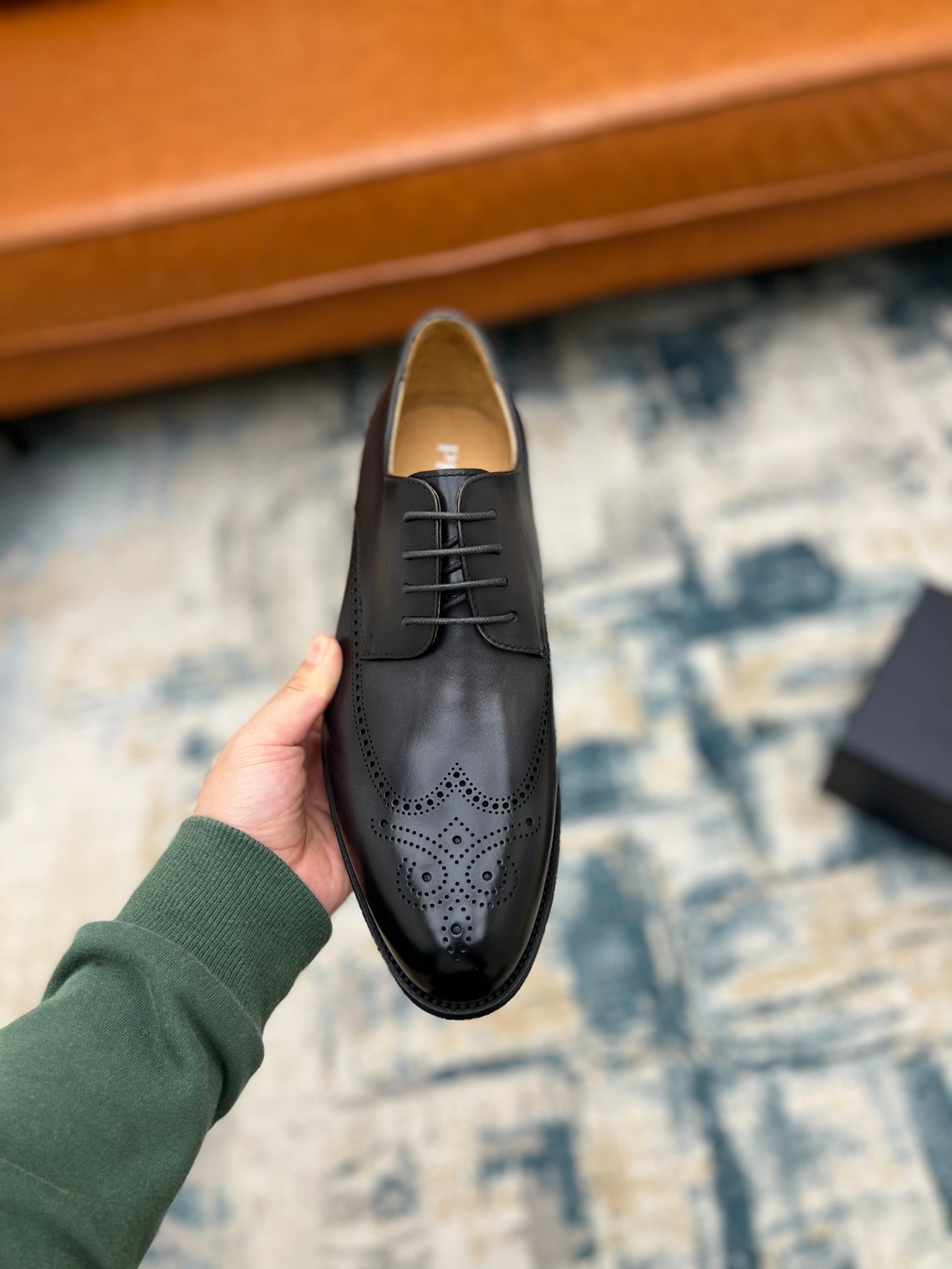 Prada unisex lace-up oxford shoe, dark leather with brogue perforations, held upright