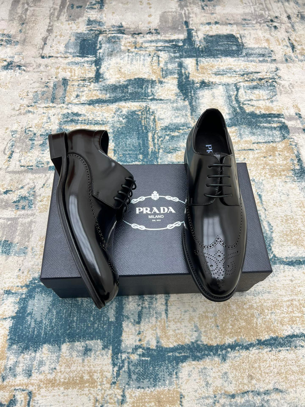 Black leather lace-up derby shoes with perforated toe, open on box