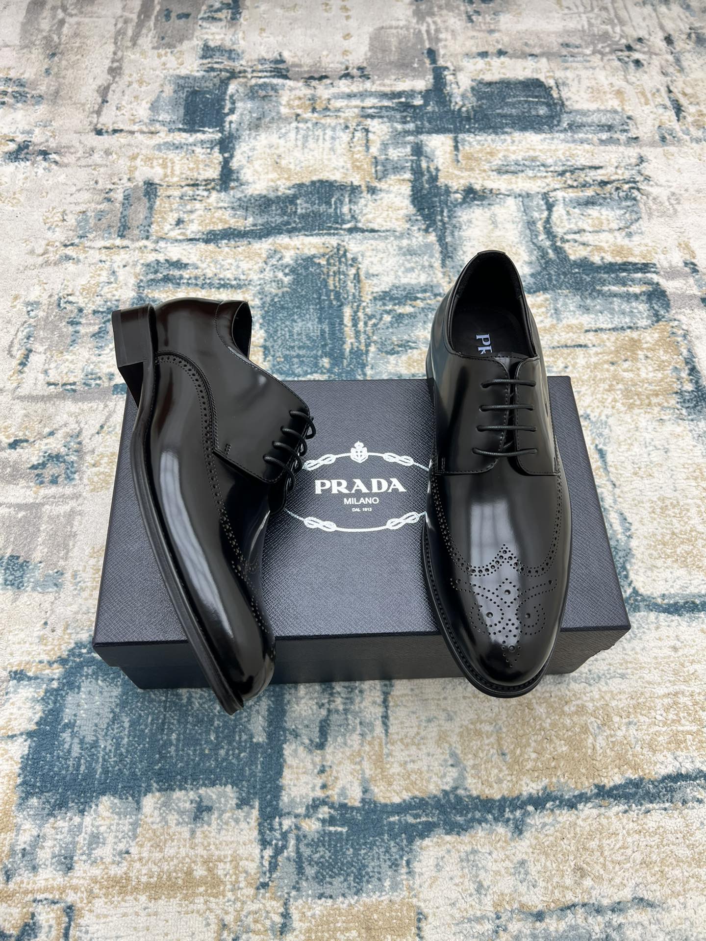 Black leather lace-up derby shoes with perforated toe, open on box