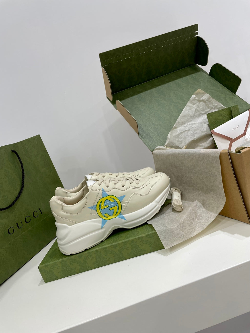 White Gucci unisex sneakers with blue-yellow star logos on side, front view