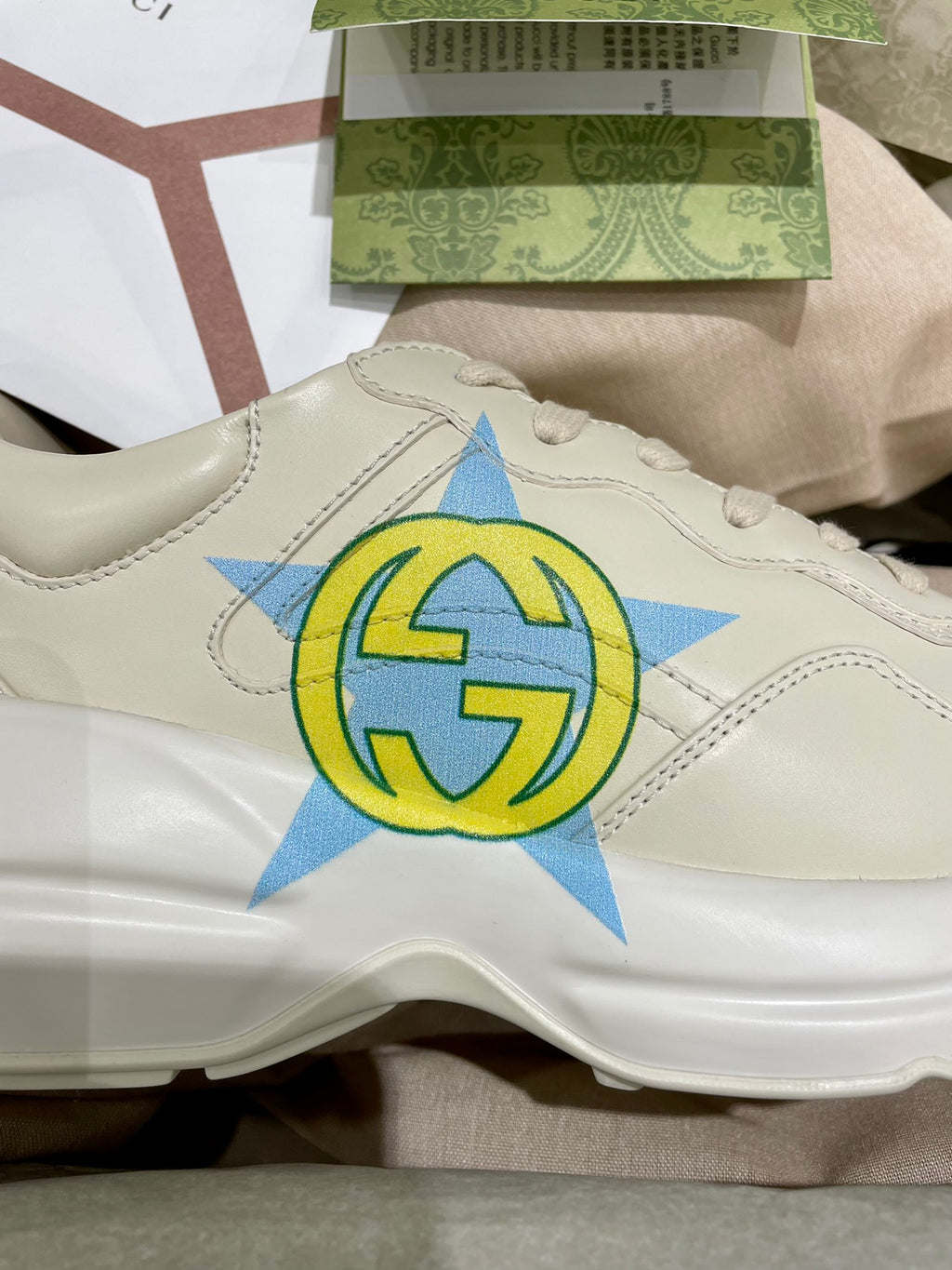 White Gucci unisex sneaker close-up with blue and yellow star logo on side