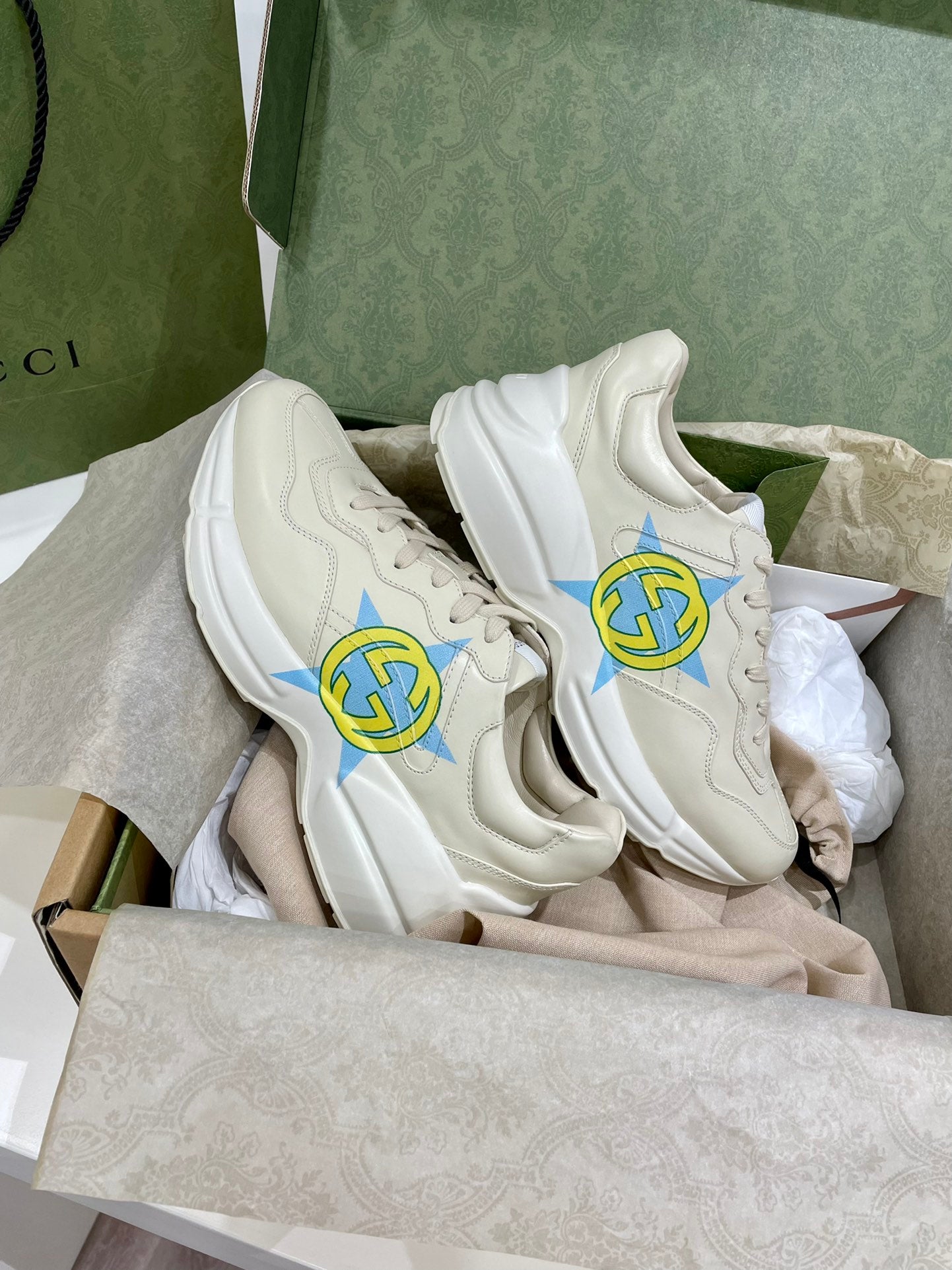 Pair of white Gucci unisex sneakers with blue-yellow star logos and laces