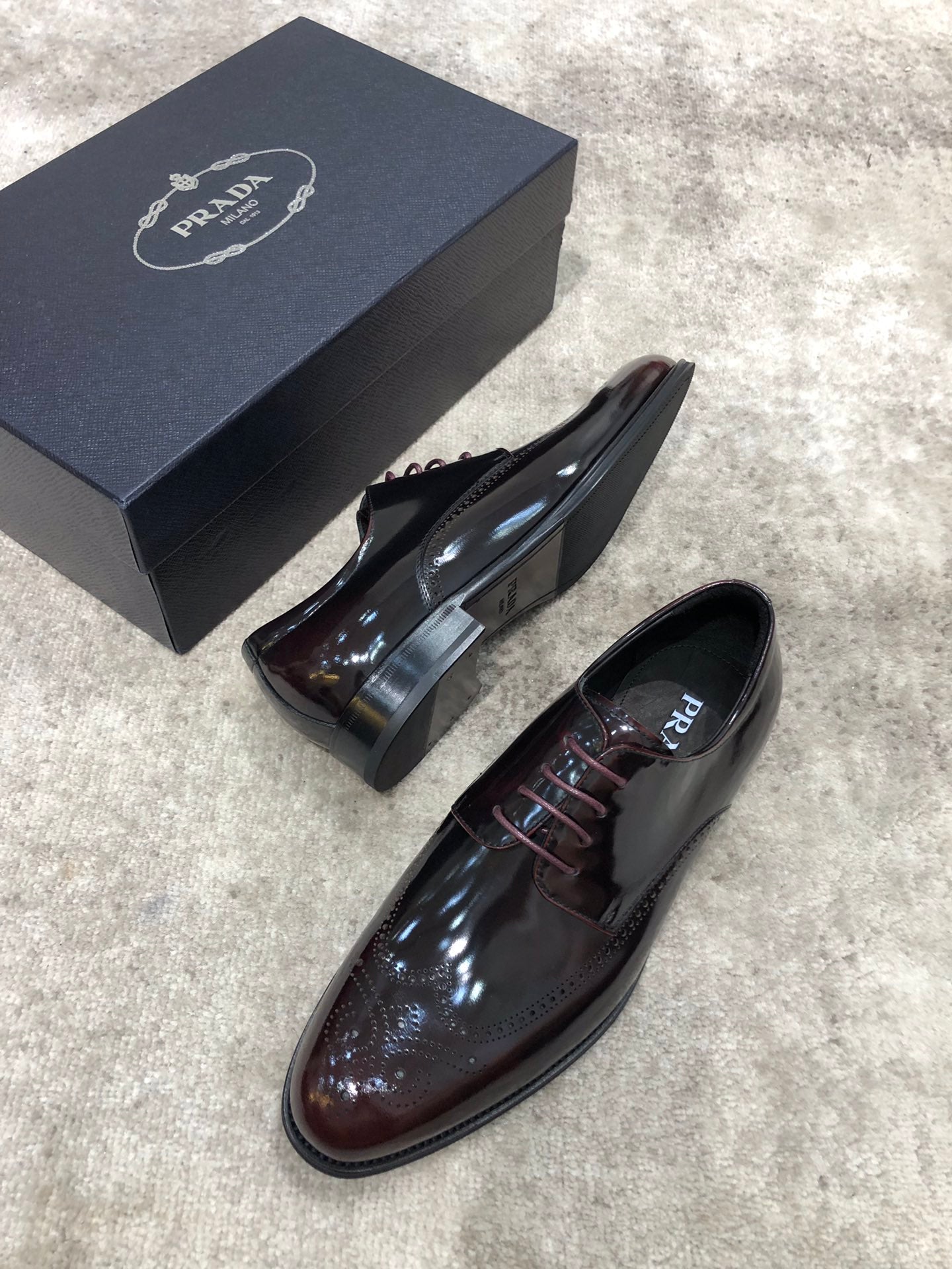 Prada lace-up dress shoes in dark brown patent leather, close side angle with box