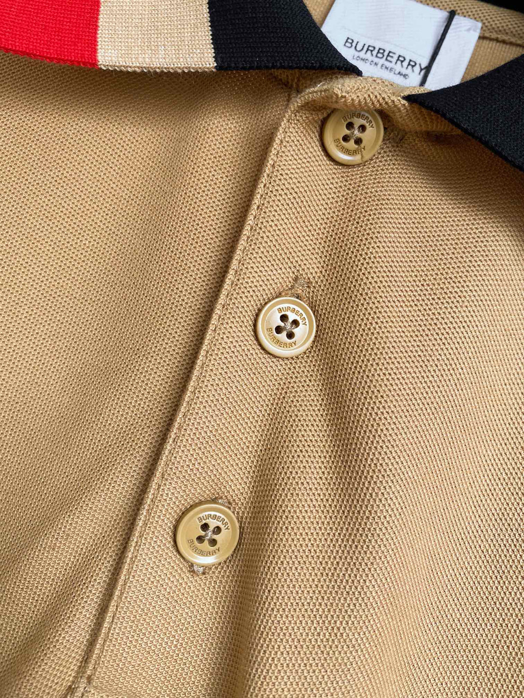 Beige Burberry polo fabric close-up with round logo buttons on placket