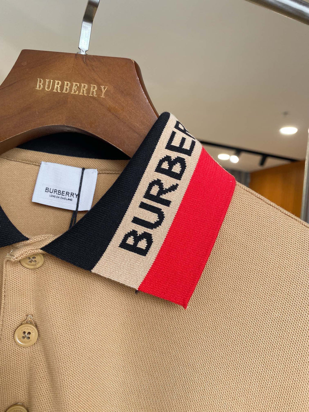 Beige Burberry polo collar close-up with red and navy logo stripe and buttons