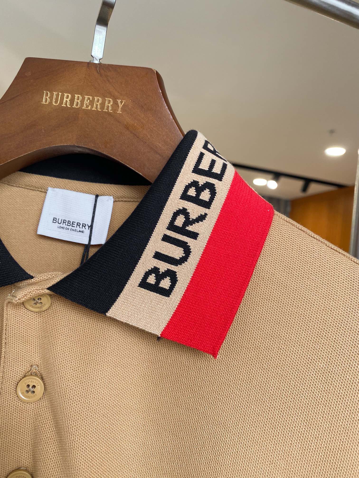 Beige Burberry polo collar close-up with red and navy logo stripe and buttons