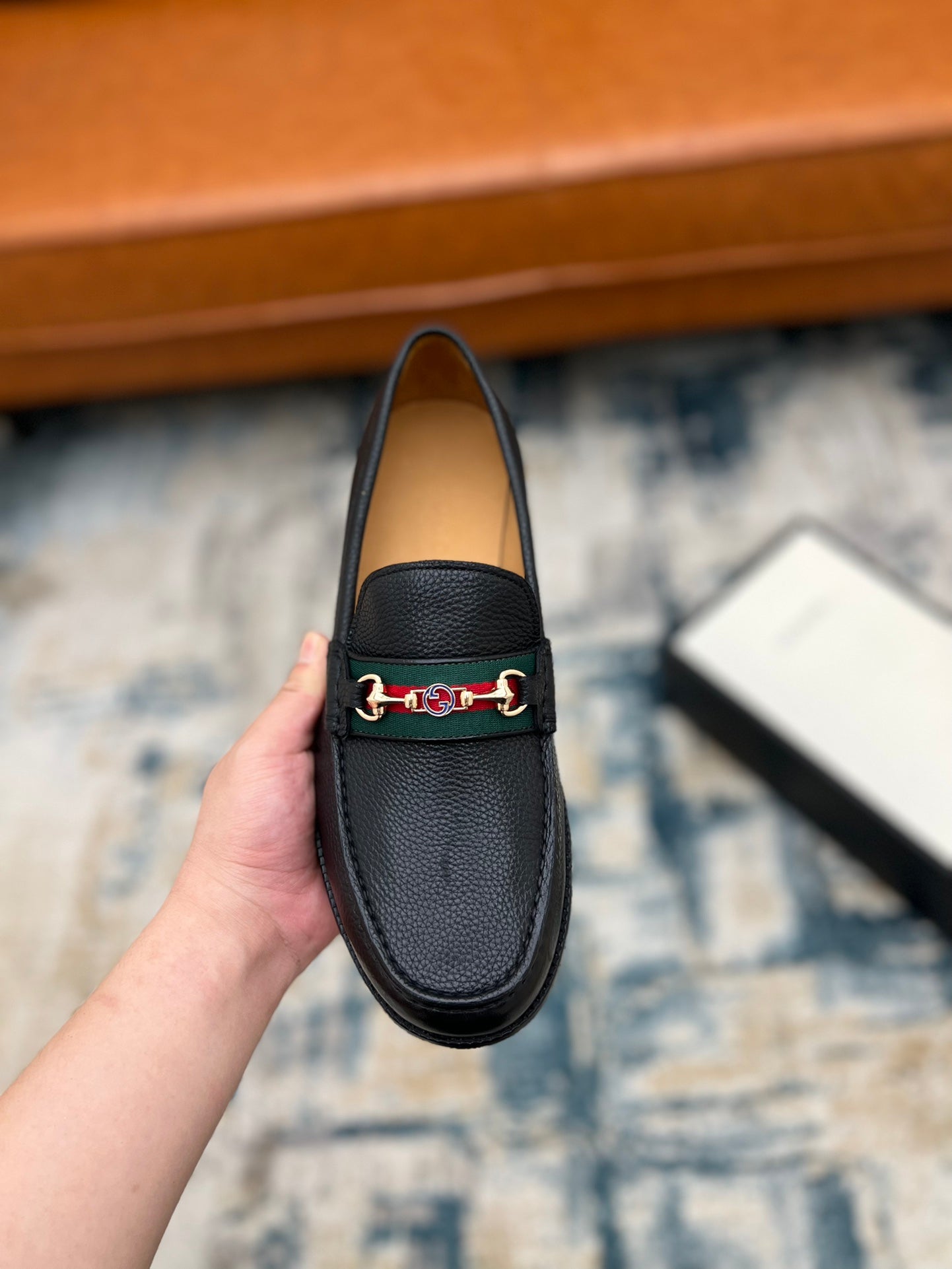 Black leather Gucci unisex loafer with horsebit detail, front view held up