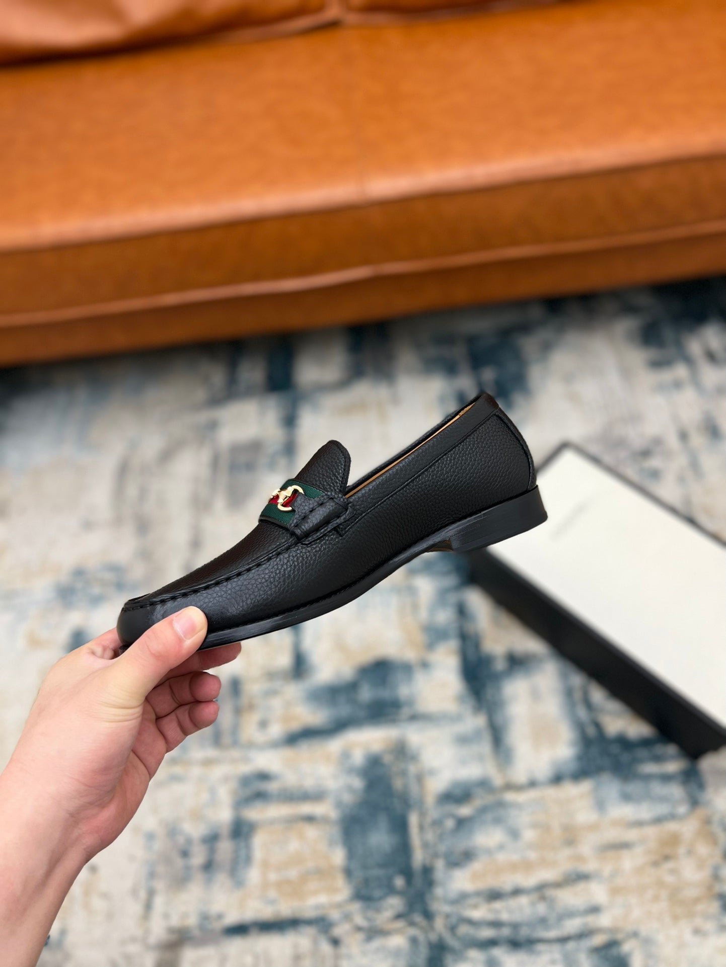 Black leather Gucci unisex loafer with horsebit detail, side view held in hand
