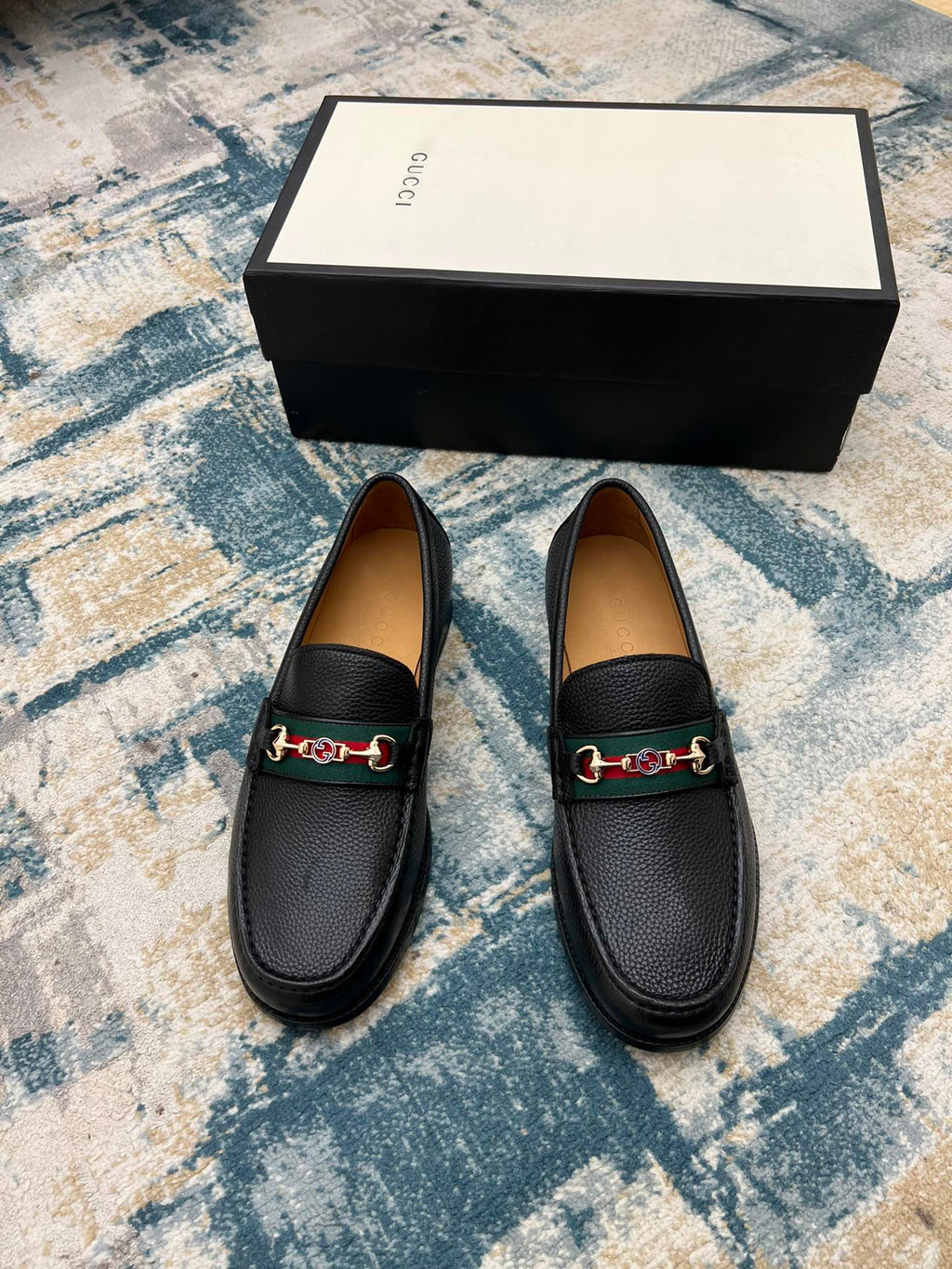 Black leather Gucci unisex loafers with horsebit detail, pair on floor by box