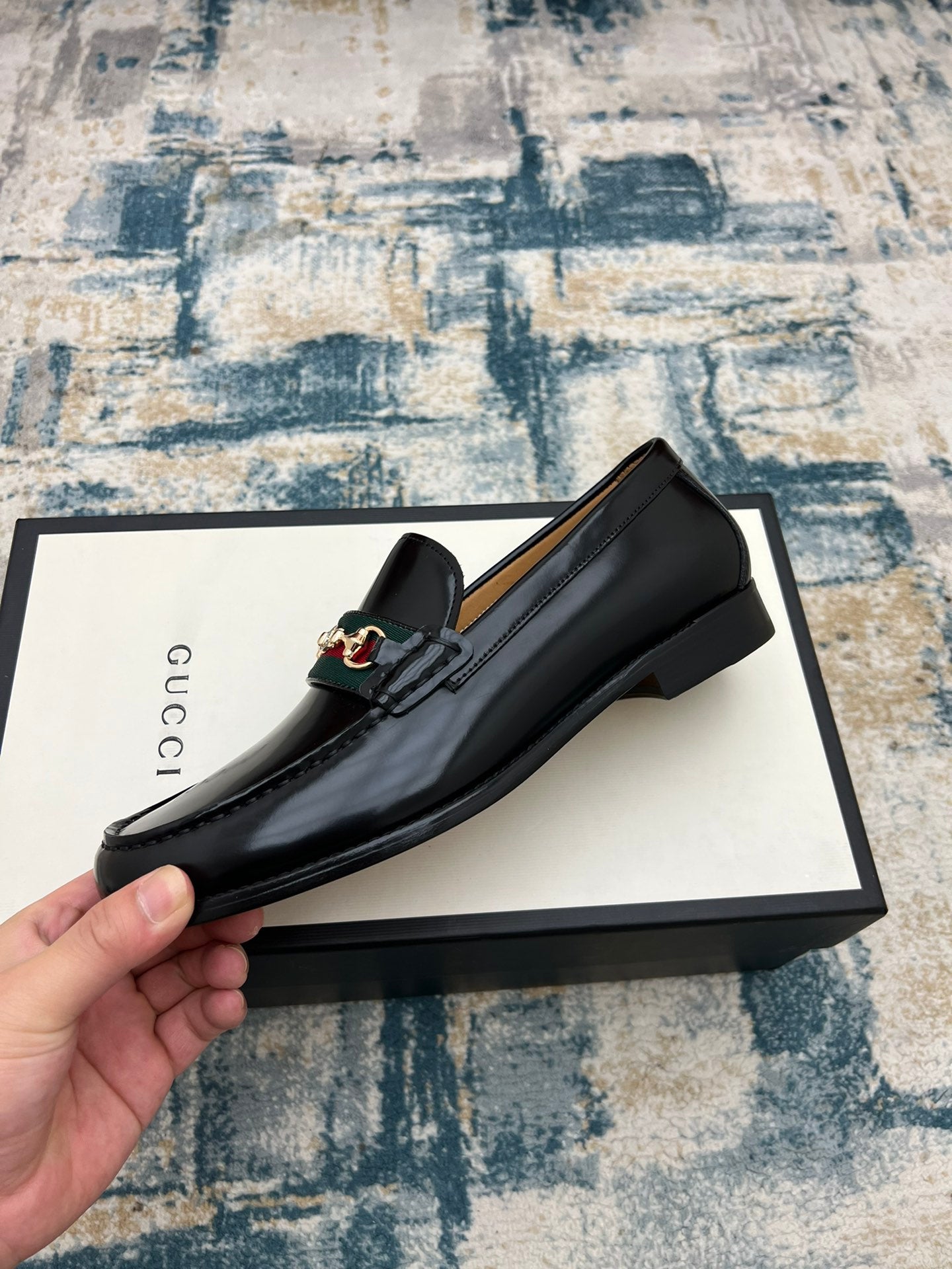 Black Gucci unisex loafer with horsebit detail on the side, held above the box