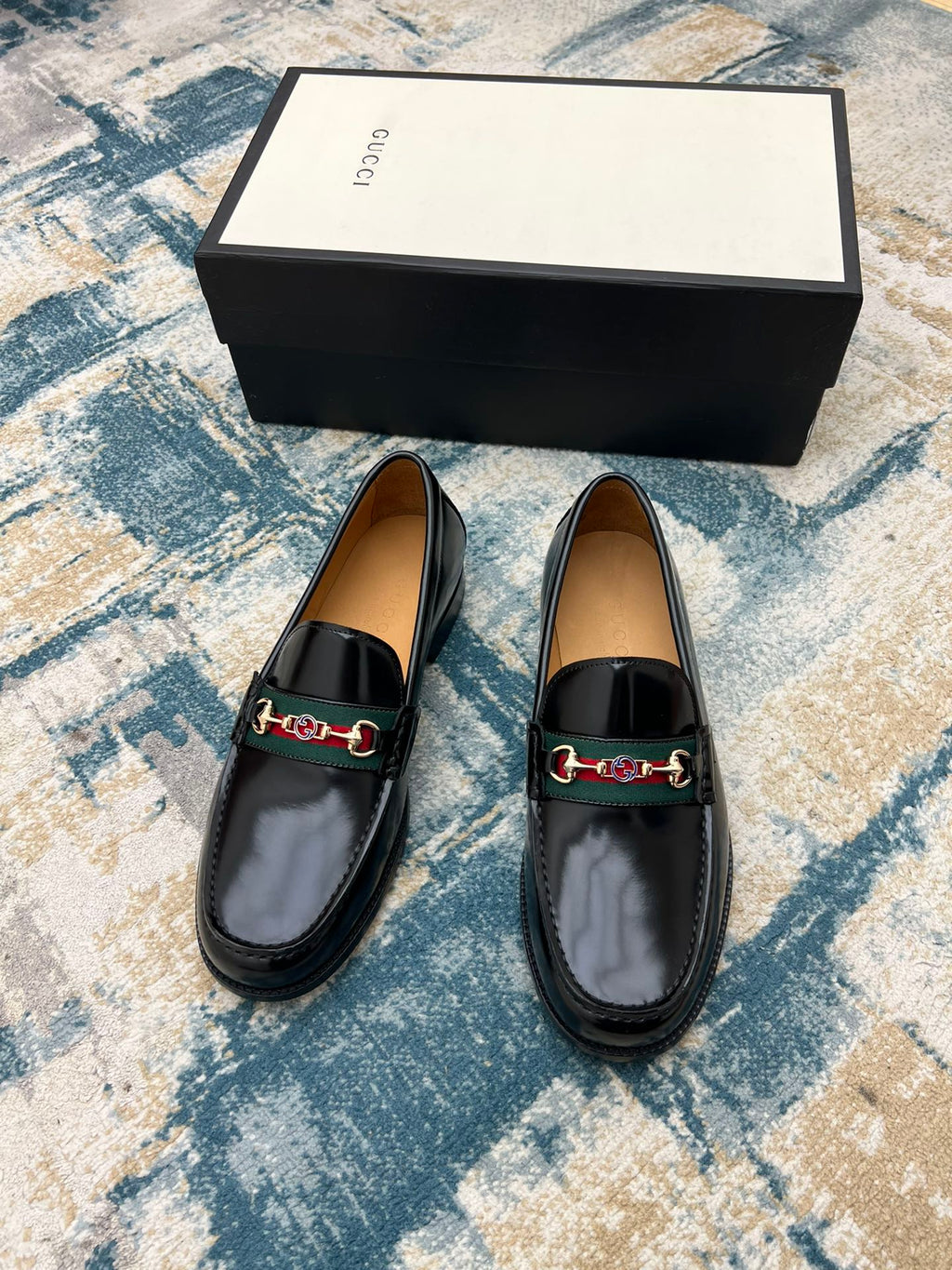 Black Gucci unisex loafers with horsebit strap detail, shown front view on a display box