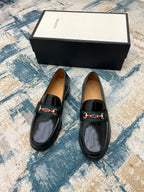 Black Gucci unisex loafers with horsebit strap detail, shown front view on a display box